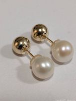 Close-up of a pair of yellow 10KT gold reversible earrings with white freshwater pearls on a white background.