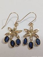 Front view of the pair of 14KT gold earrings featuring floral design with three oval blue sapphires dangling.