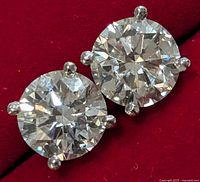 Close-up of both round brilliant lab diamonds with prong settings on red velvet background