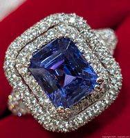 Front close-up of emerald-cut blue-violet tanzanite stone surrounded by two halo rows of round cubic zirconia.