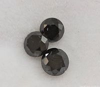 Photo showing three faceted round black diamond gemstones on white background.