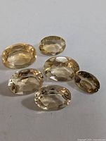 Set of six oval faceted citrine gemstones in varying pale yellow shades on white background.