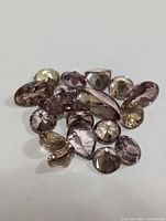 Close-up of multiple loose faceted color change garnet gemstones in various shapes and sizes on a white background.