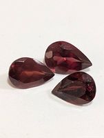 Three deep red pear-shaped garnet gemstones arranged on a white background showing facets and color.