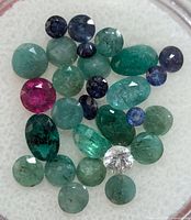 Close-up photo of multiple faceted gemstones in green, blue, pink, and white colors showing inclusions and clarity variations.