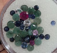 Close-up image showing loose mixed gemstones including emeralds, sapphires, rubies, pink sapphire and diamond