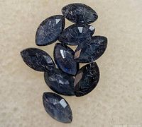 Close-up image of the marquise-shaped dark blue faceted sapphires on a white cushion.