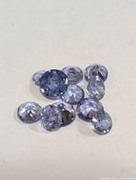 Photo showing nine round cut genuine tanzanite gemstones in different light bluish-purple shades.