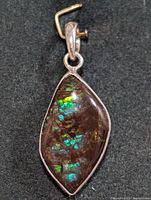 Close-up of front side of silver pendant with marquise-shaped Ammolite stone showing green and blue iridescent play of color.