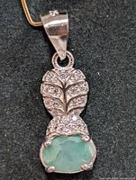 Close-up front view of the silver pendant showing the emerald and cubic zirconia details on a black background.