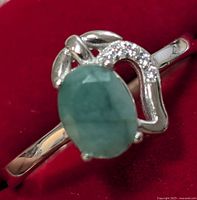 Silver ring with oval emerald and cubic zirconia stones set on a polished silver band on a red background.