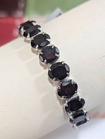 Close-up angled view of garnet bracelet showing oval garnet stones in silver setting displaying detail of stones and prongs.