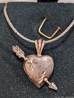 Close-up photo of the silver necklace chain and heart-shaped pendant intersected by an arrow with star engraving details.