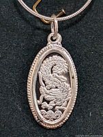 Close-up image of the silver pendant showing detailed dragon design and beaded border.