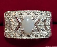 Close-up front view of silver ring with oval opal center stone on red fabric background.