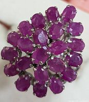 Close-up front view of a silver ring displaying a cluster of 21 oval ruby stones in a floral arrangement.