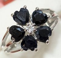 Close-up image showing the top view of the silver ring with five heart-shaped dark blue sapphires arranged around a central white topaz gemstone.