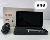 DSC touchscreen security panel with power cable and original box, showing front of device and included accessories.