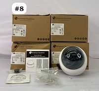 Four sealed American Dynamics surveillance cameras in original brown boxes with one dome camera displayed outside its box alongside installation accessories and manual.