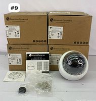 Dome style camera out of box with accompanying accessories including mounting screws, installation disk, and manual displayed in front of four original camera boxes.