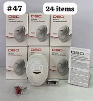 Set of 24 DSC Wireless PIR Motion Detectors PG8904P with packaging, battery, screws, and manuals arranged for display.