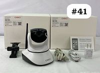 Two DSC wireless IP cameras with white bases and black lens modules, along with two white network cables, a power adapter and a USB charging cable, displayed on a gray surface with original boxes behind.