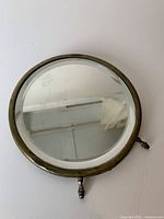 Front view of the round brass framed mirror showing reflective surface and tarnished brass frame with a stand/base fixation.