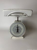 Front view of distressed white Hanson antique kitchen scale showing circular dial face and metal weighing platform.