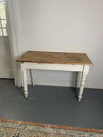 View of antique pine farmhouse table with raw wood top and painted white base, placed against a wall.