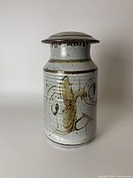 Front view of handmade pottery canister showing abstract brushstroke design on light grey glaze with fitted lid.