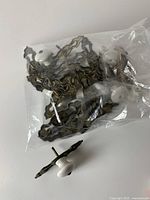Bag containing several brass backplates with attached white ceramic knobs, plus one separate knob with backplate out of the bag.