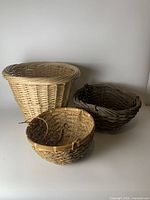Photo showing all three baskets: a large natural wicker basket without hanging chains, and two hanging baskets, one natural wicker and one dark brown wicker, each with attached hanging chains.