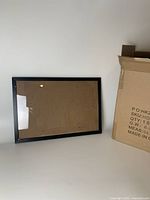 Single black picture frame showing the front with plexiglass and backing, displayed against a wall.