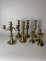 Full frontal view showing all eight brass candlesticks in varying designs including the large three-arm candelabra and three pairs of candlesticks with different base shapes.