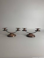 Pair of handmade copper candlesticks with double taper holders and round bases shown from front