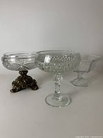 Three pedestal dishes of varying styles: one with brass decorative base and cut glass bowl, one cut glass compote dish, and one square glass dish on pedestal.