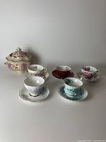 Photo showing the five fine china cup and saucer pairs and the tureen with lid, all with floral patterns and gold accents.