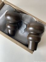 Box containing two unused IKEA Viskafors furniture feet showing the dark wood shape and rounded design packed in protective foam.