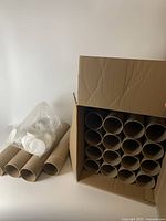 Box containing multiple cardboard tubes arranged vertically with some white plastic lids visible alongside.