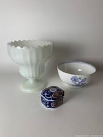 Three decorative items on a table: white milk glass vase, blue and white bowl, small chinoiserie trinket box