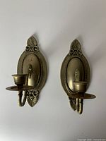 Pair of solid brass wall sconces with oval backplates and decorative leaf and scroll motifs.