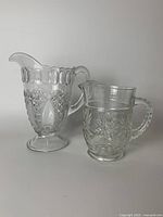 Photo of two clear pressed glass pitchers showing different embossed patterns and handles.
