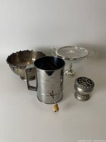 Photo showing all four items: silver flower frog, flour sifter, large silver bowl, glass pedestal dish with silver handles.