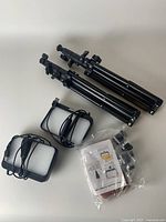 Overview photo showing two rectangular LED video lights with USB cords, two black adjustable tripods, and a sealed bag containing color filters and mounting accessories.