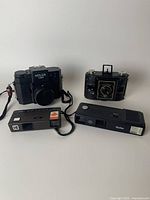 Four vintage film cameras including Holga 120N medium format, Kodak Clipper folding camera, Vivitar compact camera and Kodak compact camera with maple leaf logo