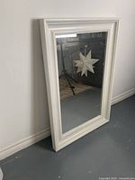 Full view of the white framed rectangular mirror standing against a wall, showing the overall design and size relative to the wall baseboard