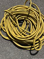 Coiled yellow rubber hose laid out on paved surface, showing general length and condition.