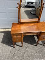 Front angle view of antique vanity showing wood grain pattern, drawers, and mirror with turned legs.