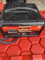 Top view of black battery charger with handle, showing vent slots and general shape.