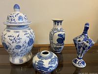 Full set of four blue and white porcelain vases and jar shown together on glass table with wood frame.